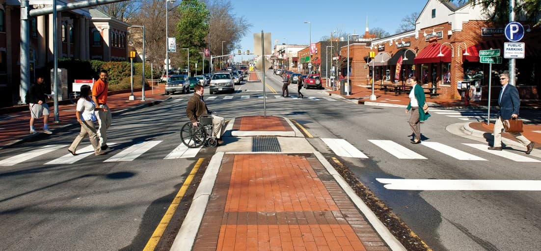 Pedestrians use a marked crosswalk to cross two vehicle lanes separated by a median.