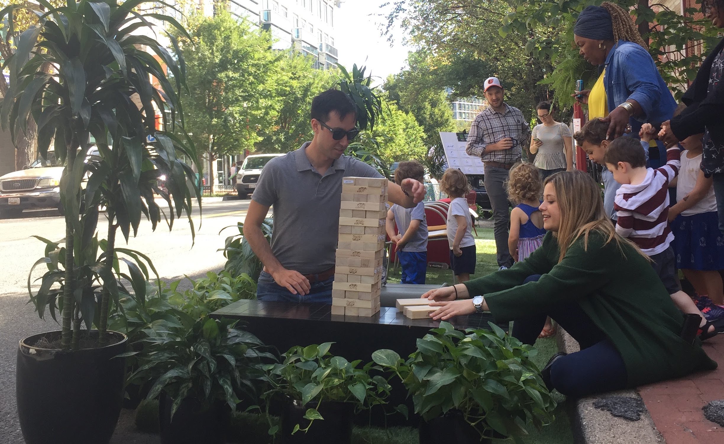  /></p>
<p>In 2005, three collaborators tested a new idea—they turned an underutilized and heavily subsidized piece of land (a parking spot) into a useful space with some grass, a bench, and a potted tree. People started using it almost immediately. Since posting the first picture of this DIY mini-park in San Francisco, this experiment in urban design has morphed into a global phenomenon. Now, hundreds of cities around the world hold PARK(ing) Day on the third Friday in September where dozens of parking spots that are usually reserved for stationary, empty cars are transformed into places for people.</p>
<p>According to John Bela, one of the brains behind the park that started it all, “it wasn’t necessarily about protest, but it was about demonstrating an alternative to storing cars in parking spaces.” It’s an important point. Cities—especially in North America—devote an insane amount of public space to storing empty, voluminous private vehicles. A recent study of parking shows that “car storage has become the primary land use in many city areas,” and at great expense.</p>
<p>Policies that require an excessive amount of parking for new development, based on unrealistic standards, can dramatically drive up the cost of housing or business space. And devoting 9-18 feet of street space for on-street parking takes up a lot of land that could otherwise be used for wider sidewalks, bike/scooter lanes, rain gardens, and—as PARK(ing) Day illustrates—many other public uses.</p>
<p>Below are a few of the “parklets” scattered around our office in Washington, DC and what their creators had to say about them.</p>
<h4><span style=