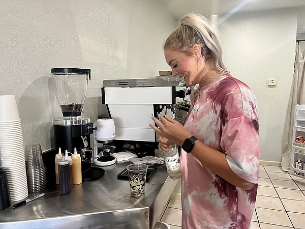 Prepping lattes looks like fun as a student laughs and opens up a bottle of vanilla syrup in the back of the cafe